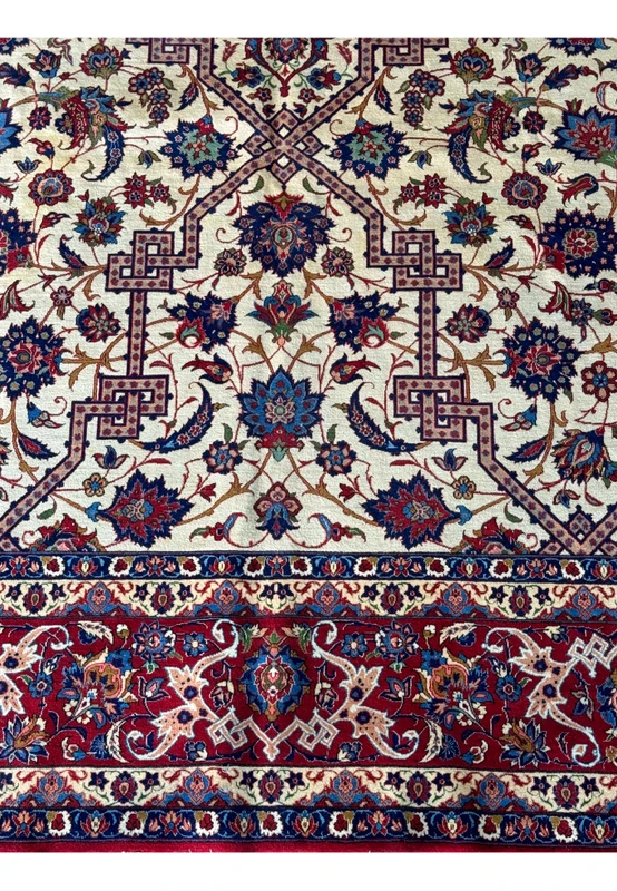 ull view of the Persian Isfahan rug on a flat surface highlighting the detailed overall pattern with a creamy ivory background and red borders.