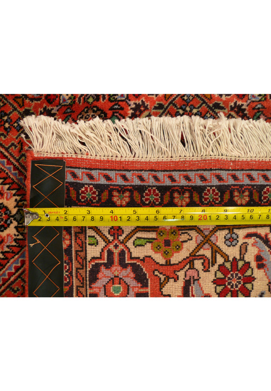 A ruler laid across the backside of the rug, measuring the knots' density, with the yellow measuring tape providing a scale that highlights the tightness of the weave, essential for the rug's resilience and quality.