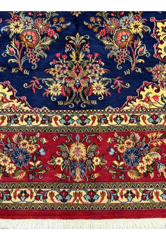 Close-up view of the middle lower border of a Persian Qum Kork rug, showing a detailed display of traditional floral motifs in a variety of colors like red, blue, cream, and gold on a deep navy background, exemplifying the rug's dense pattern work