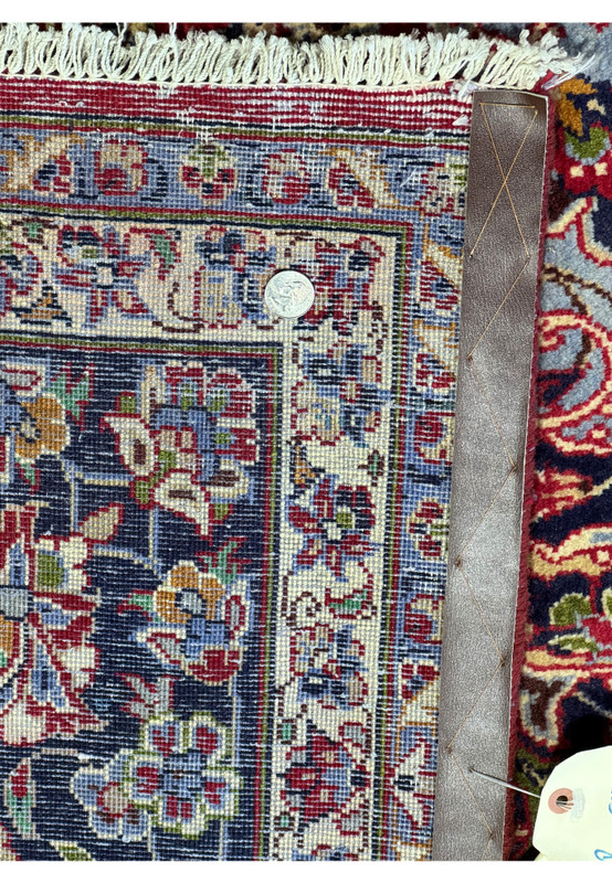 Detailed view of the edge and back of a Persian Isfahan rug with measuring tools - This image displays the edge and back side of the Persian Isfahan rug. A leather runs along the side, illustrating the rug's meticulous craftsmanship and durability. The quarter on the rug serves as a reference for the scale, showcasing the tight, consistent weaving and vibrant coloration that characterize the rug's superior quality.