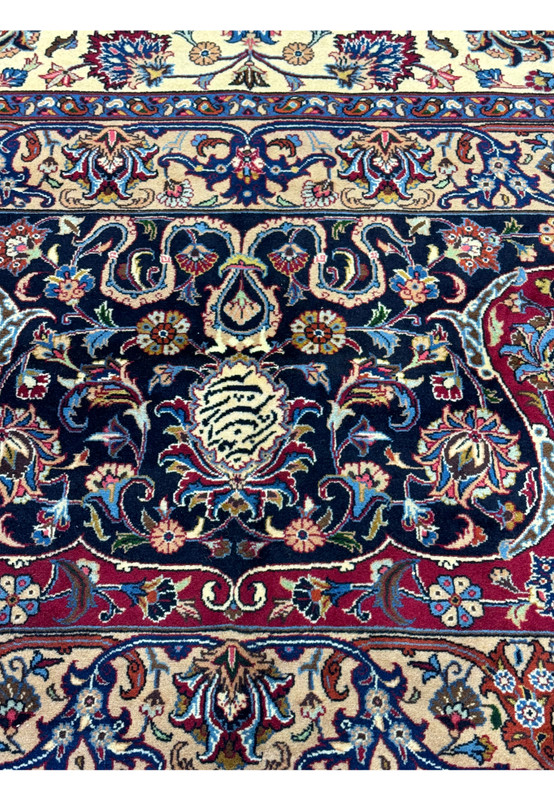 Close-up view of intricate floral and vine patterns on a Persian Mashad rug, highlighting the detailed craftsmanship with vibrant colors including deep red, blue, and ivory, showcasing traditional Persian design elements.