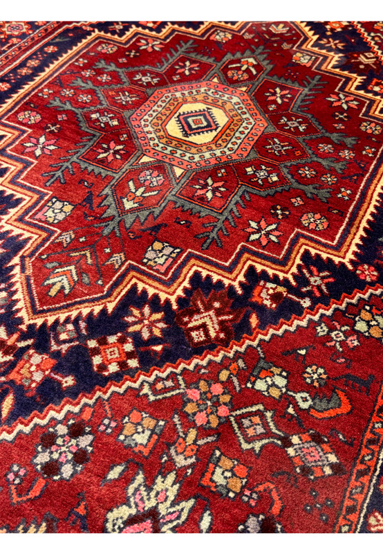 Close-up of the bottom section of a 3'4" x 5'1" Persian Gholtogh Rug, showcasing the intricate floral and geometric patterns in the border. The vibrant red field and navy blue accents highlight the detailed craftsmanship and traditional design elements of this hand-knotted wool rug.