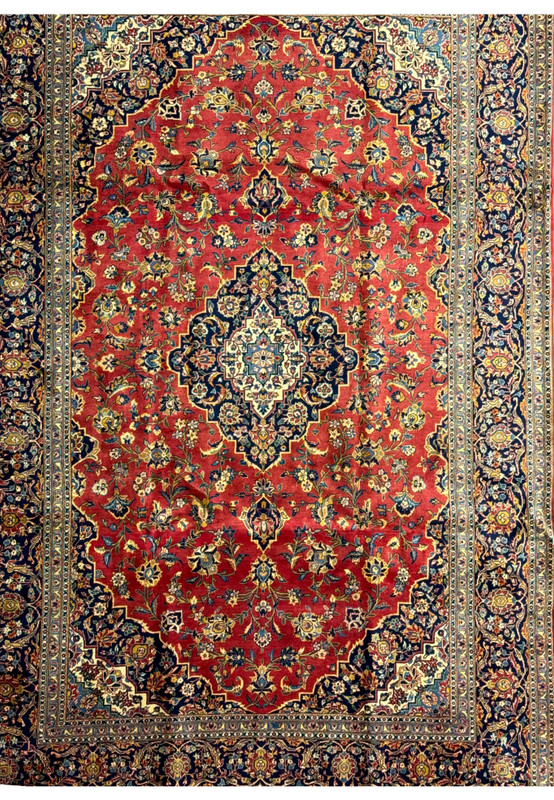 Detailed shot of the central medallion on a Persian Kashan rug. The medallion features a complex design with layers of floral motifs and geometric shapes in shades of blue, gold, and ivory against a red field. The precision of the knotting and the clarity of the design highlight the skill involved in creating this luxurious rug. This close-up emphasizes the artistic quality and cultural heritage embedded in Kashan rugs.