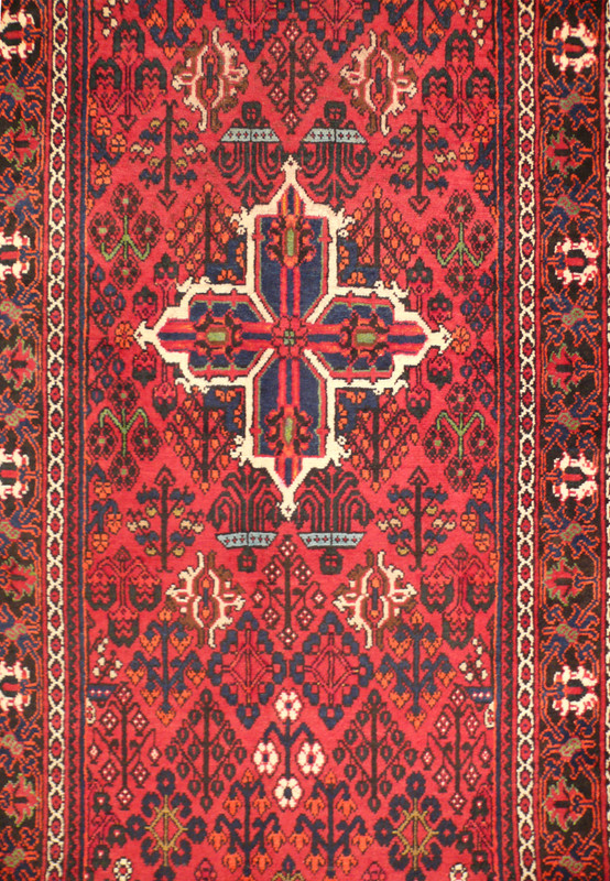 Close-up of the central medallion on the Persian Meymeh runner rug, emphasizing the detailed floral and geometric patterns. The deep red background is complemented by blue, ivory, black, and green accents, showcasing the rug's intricate design.
