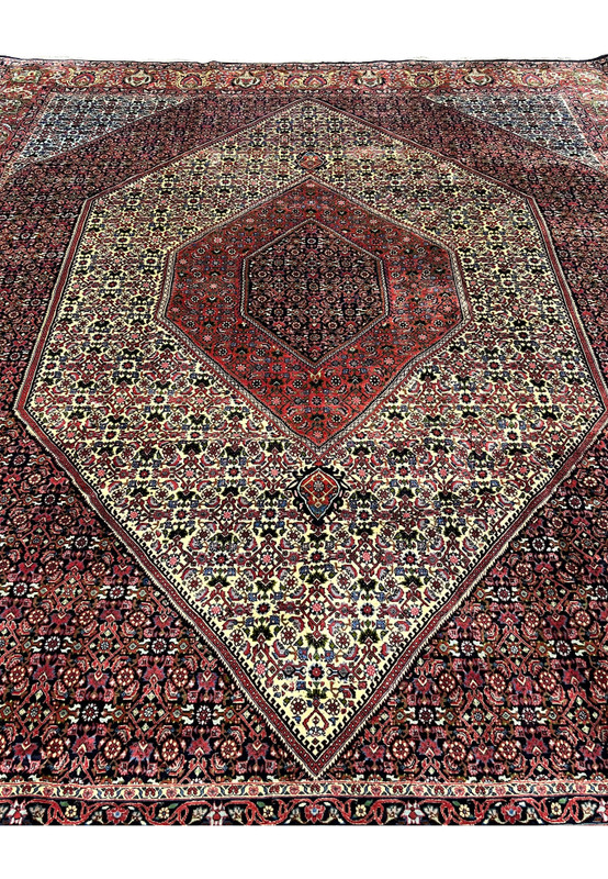 Angled perspective of a 9.8 x 12.2 Persian Bijar rug showing dense hand-knotted wool, rich red tones, ivory field sections, and the rug’s heavy iron-weave construction.