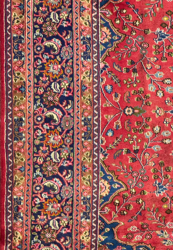Perspective view of the Persian Mashad rug showing its overall design and detailed border.