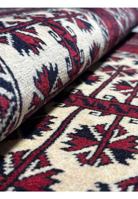 Rolled view of a 3'1 x 4'2 Persian Baluch rug, emphasizing the soft wool pile and the detailed star and geometric motifs in red, blue, and ivory