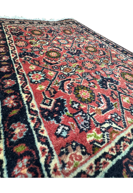 Angled view of the 1'3 x 2' Persian Baby Bijar Rug showing its intricate patterns and vibrant red background.