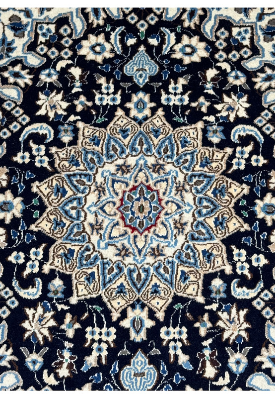 Close-up of the central medallion on a Persian Nain rug with intricate floral patterns in navy blue and ivory.