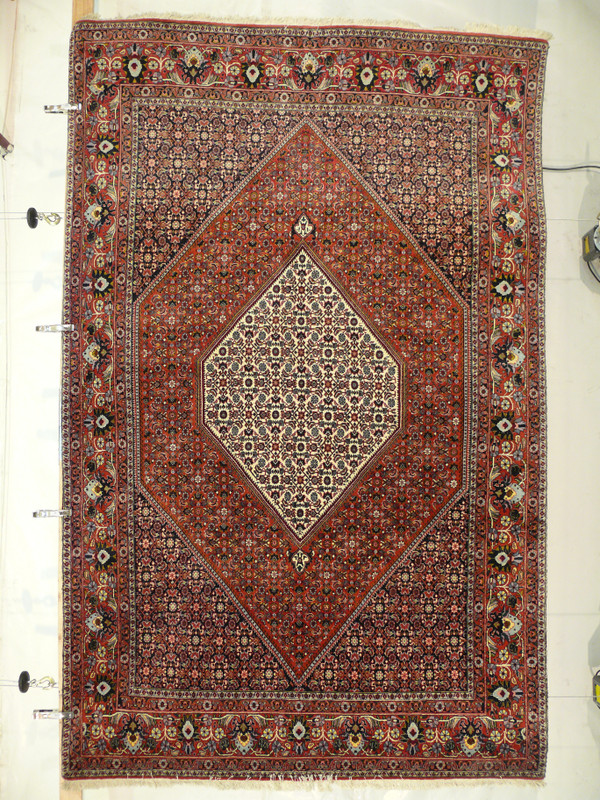 Hanging view of 6'9 x 9'4 Bijar Persian Iron Rug with brick red field, ivory medallion, and floral motifs