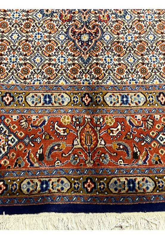 Lower border detail illustrating the intricately knotted floral vine motifs in rust, navy, and beige, bordered by a navy frame and fringed white tassels.