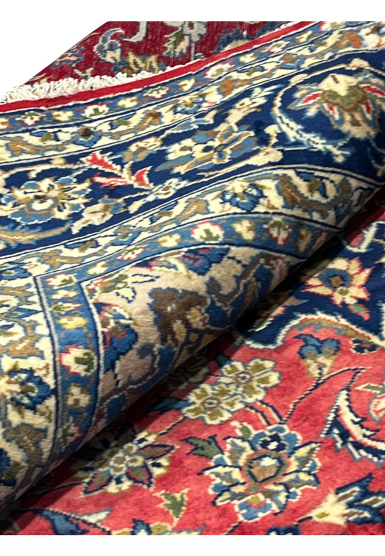 Rolled view of the 8'7 x 12'7 Distressed Persian Isfahan Rug emphasizing the hand-knotted floral pattern, navy border, and fine wool pile with visible craftsmanship.