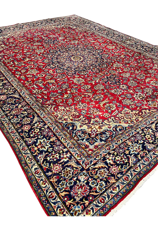 Angled view of 9'10 x 13'1 Persian Isfahan rug displaying medallion, floral designs, ruby field, and navy borders