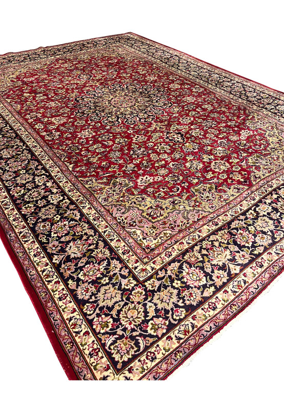 Angled view of large red Persian Isfahan rug showing navy floral border and medallion