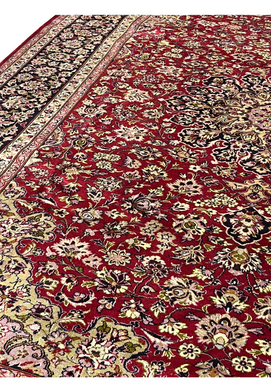 Close-up of floral patterns on red Persian Isfahan rug showing detailed blossoms, scrolling vines, and soft pastel highlights across the field.