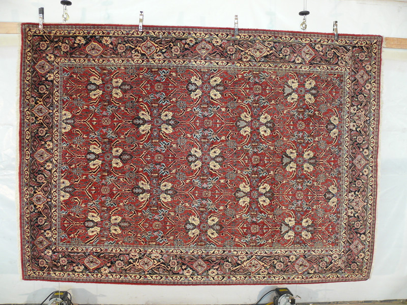 Hanging view of floral Bijar iron rug showing brick red background, ivory palmettes, navy vines, and dense wool texture