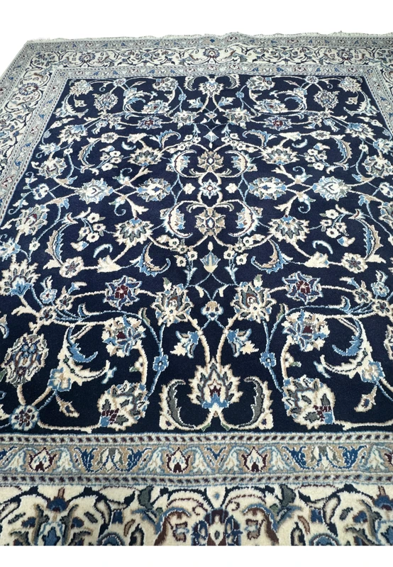 Midfield closeup of Persian Nain rug showing detailed floral vines, palmettes, and layered botanical motifs on navy background