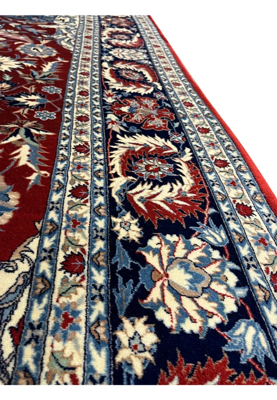 Close-up of Persian Isfahan rug border showing navy floral vines, ivory guard borders, and red field with crisp hand-knotted wool detail.