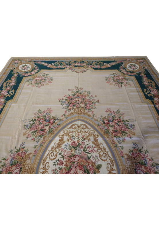 Upper section detail of French Aubusson rug highlighting emerald green border, pink rose garlands, muted gold scrollwork, and beige background