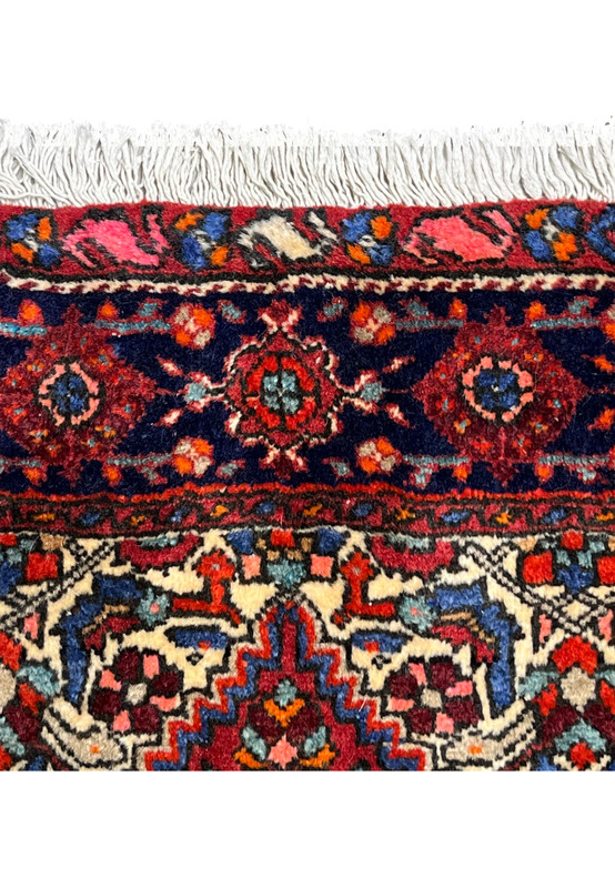 Upper border detail of a 3'4 x 4'9 Persian Gholtogh rug with dark navy border, geometric rosettes, rich reds, and hand-knotted wool fringe