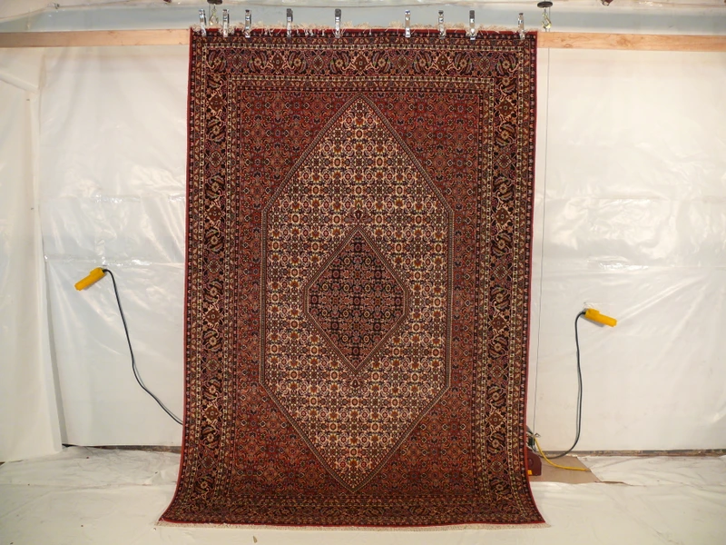 Hanging view of a 6'5 x 10 authentic Persian Bijar rug showing its firm iron rug structure, dense wool pile, crisp medallion design, and rich red color tones