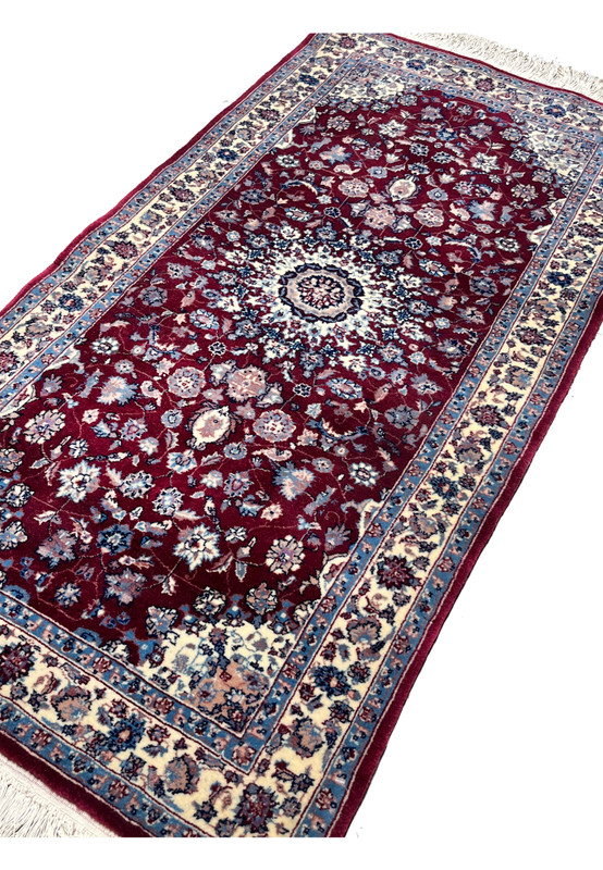 Angled perspective of a Persian Tabriz medallion rug highlighting pile texture, color depth, and the contrast between burgundy field and ivory borders