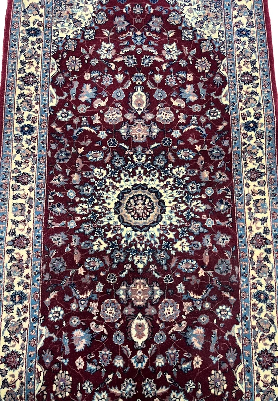 Close view of the central medallion on a Persian Tabriz rug showing ivory and navy detailing, fine knotting, and dense floral symmetry on a burgundy field.