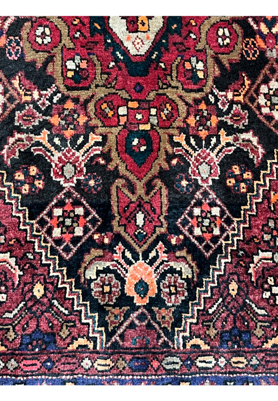 Lower section of a Persian Gholtogh rug showing medallion extension, geometric florals, rich red field, and balanced tribal composition