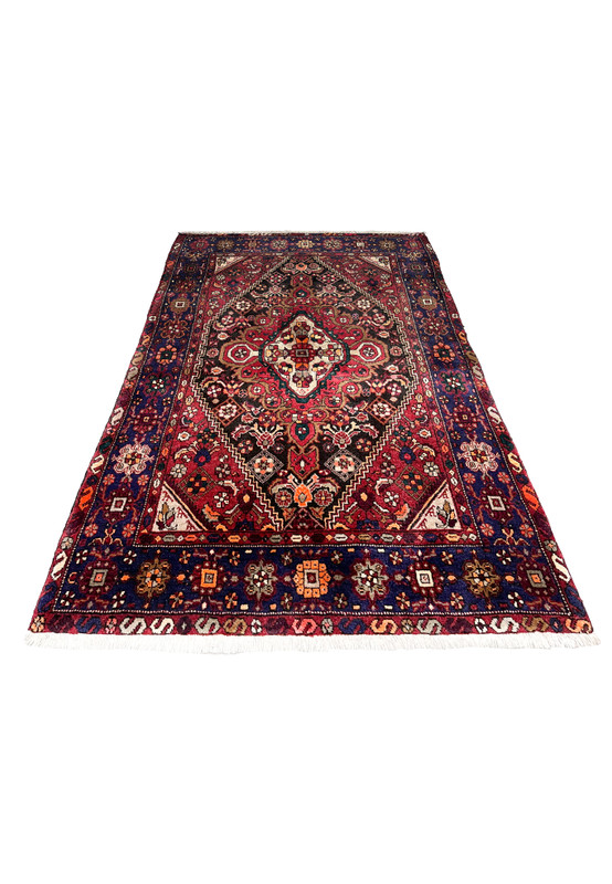 Laid flat view of a Persian Gholtogh rug showing strong geometric medallion, deep red ground, navy framing, and expressive tribal patterning