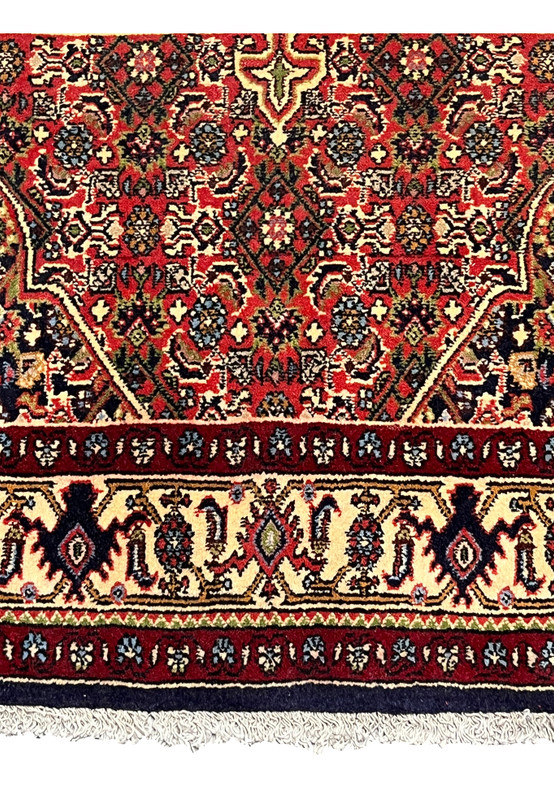 Lower border view of a Persian Bijar rug featuring layered framing, deep red tones, floral rosettes, and strong visual definition