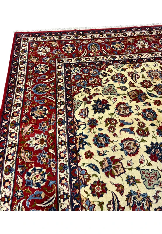 Upper border closeup of a Persian Isfahan rug featuring deep red tones, scrolling floral vines, navy accents, and elegant silk highlights