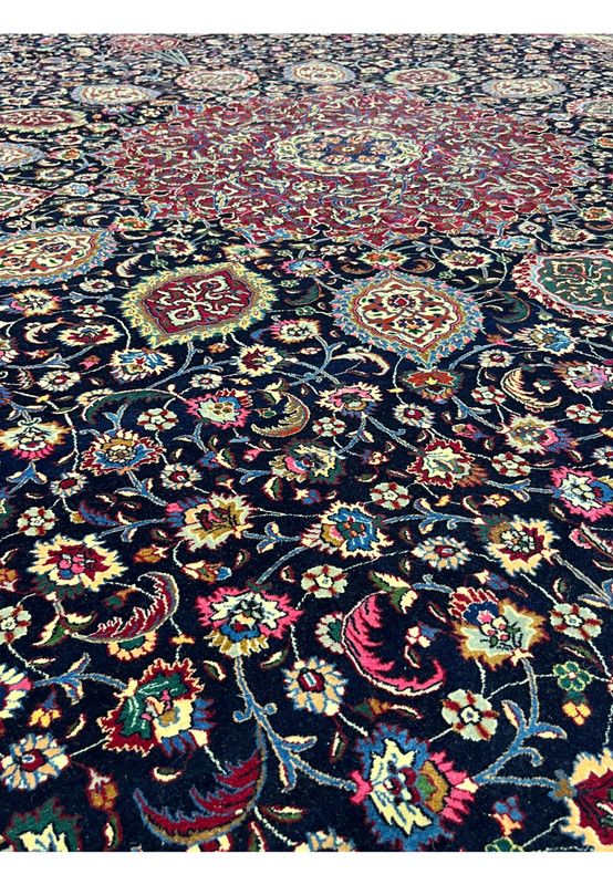 Close-up of Persian Mashad rug colors showing rich navy blue, ruby red, ivory, green, and gold tones woven in fine kork wool and silk pile