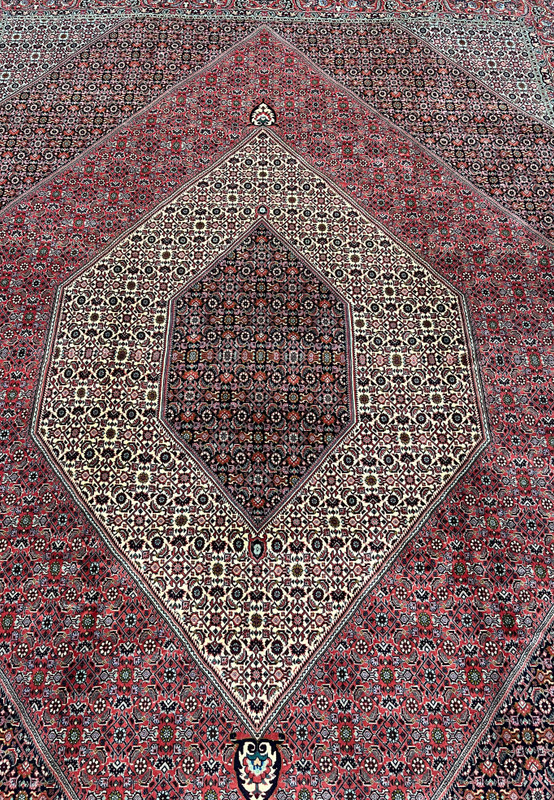 Central field detail of a Persian Bijar iron rug showing dense geometric elements, tight knotting, ivory accents, and rich brick red background
