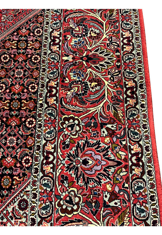 Border closeup of a Persian Bijar iron rug highlighting layered floral borders, deep red ground, navy accents, ivory details, and heavy wool construction