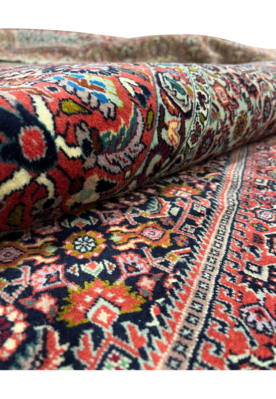 Rolled edge view of a 9x13 Persian Bijar iron rug showing dense wool pile, deep red field, navy blue details, and tightly packed geometric motifs