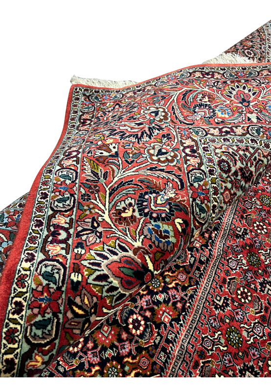 Folded corner of a Persian Bijar iron rug highlighting thick construction, crisp geometric patterns, dark navy blue ground, and rich red tones