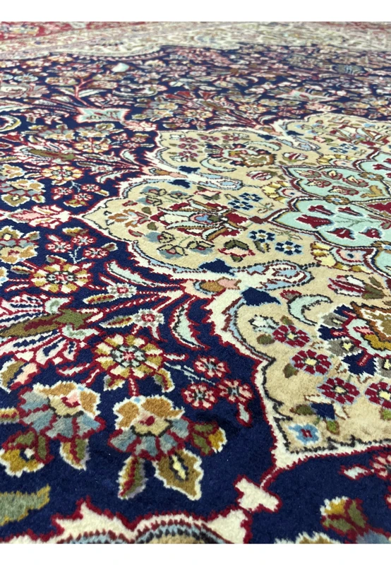 Pattern close-up of a Persian Tabriz rug featuring layered floral motifs, deep navy background, and finely detailed ivory accents