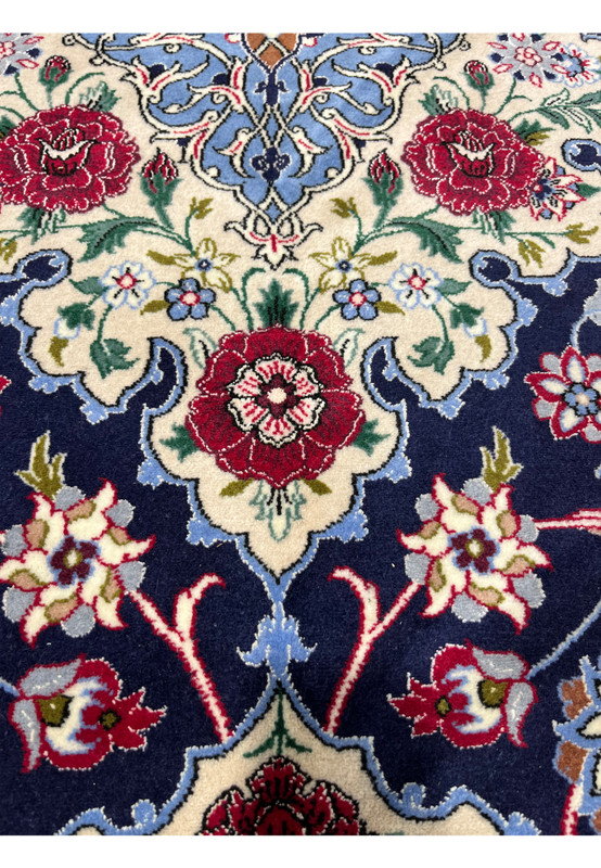 Close-up of a Persian Isfahan rug showing raised floral motifs in deep navy, burgundy red, ivory, light blue, sage green, and soft gold wool and silk