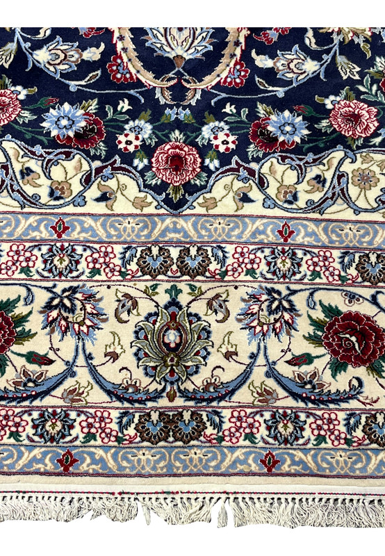 Lower border detail of a Persian Isfahan rug with scrolling floral vines in ivory, powder blue, burgundy, olive green, and navy on a finely knotted foundation