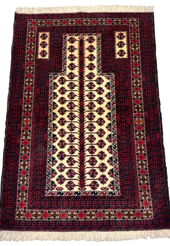 Laid-down view of a Persian Baluch prayer rug showing vertical mihrab layout, deep burgundy tones, and strong tribal pattern structure