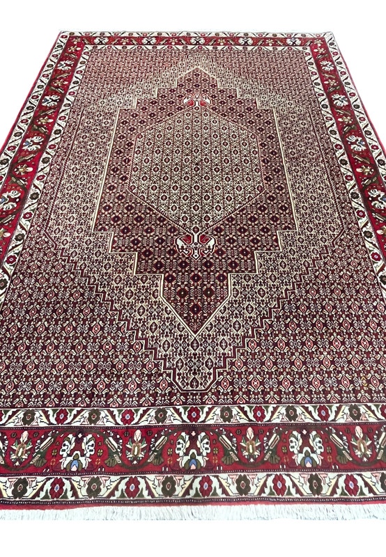 Laid flat view of Persian Senneh rug highlighting elongated medallion form, dense allover geometry, and balanced burgundy and ivory tones
