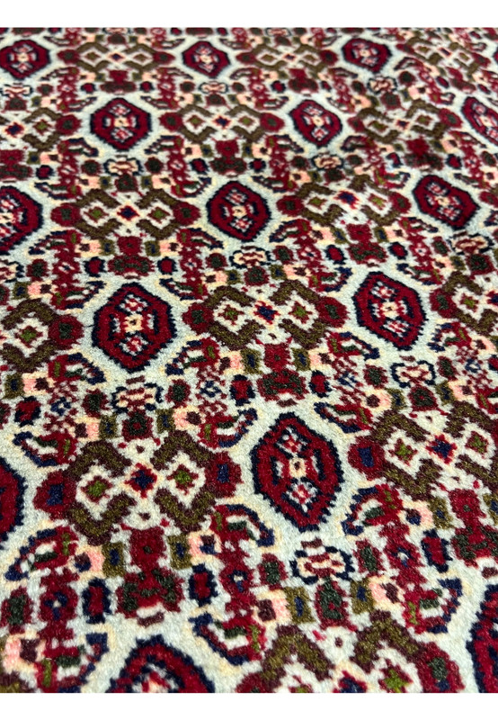 Herati inspired detail in Persian Senneh rug showing stylized rosettes, angular leaves, burgundy field, and ivory lattice definition