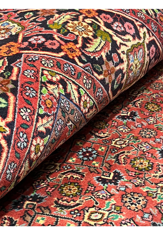 Persian Bijar all-over rug partially rolled to display rich terracotta field, navy border, and intricate floral motifs