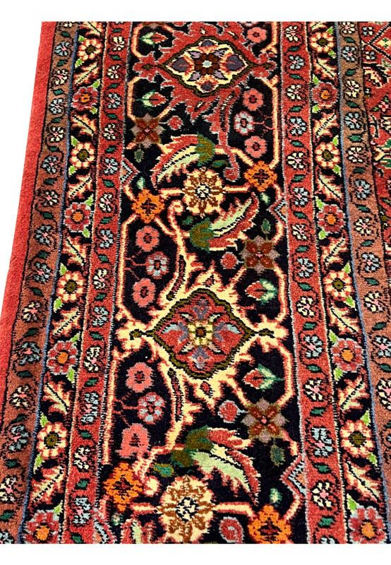 Close-up of Persian Bijar rug border with detailed floral motifs, dark navy ground, and terracotta accents