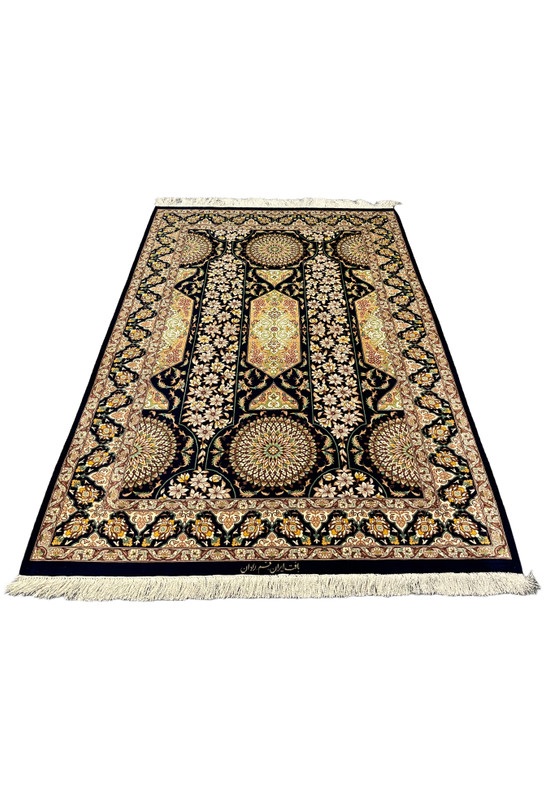 Laid down angle of signed Qum silk rug showing navy ground gold panels dense floral vines and crisp silk weave small luxury handmade Persian rug