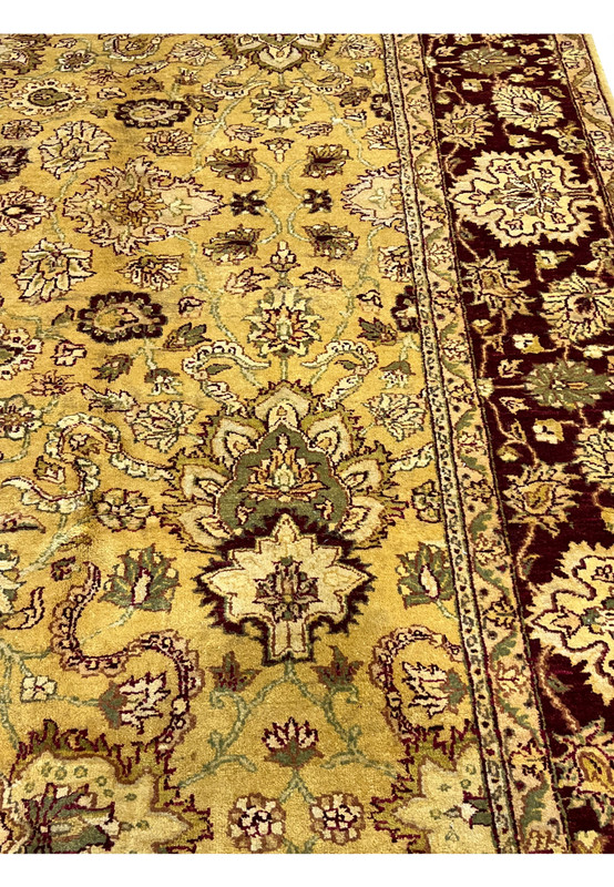 Close view of gold field Indian Agra rug showing intricate floral motifs, olive green leaves and burgundy vine outlines in handmade wool.