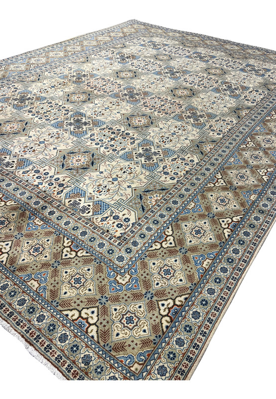 Angled overhead view of a Persian Tabriz Kheshti rug showing the complete field pattern of repeating star medallions with floral bouquets, blue checkerboard diamond compartments, and Greek-key lattice connectors, with the wide ornamental border and cotton fringe visible at the bottom edge.
