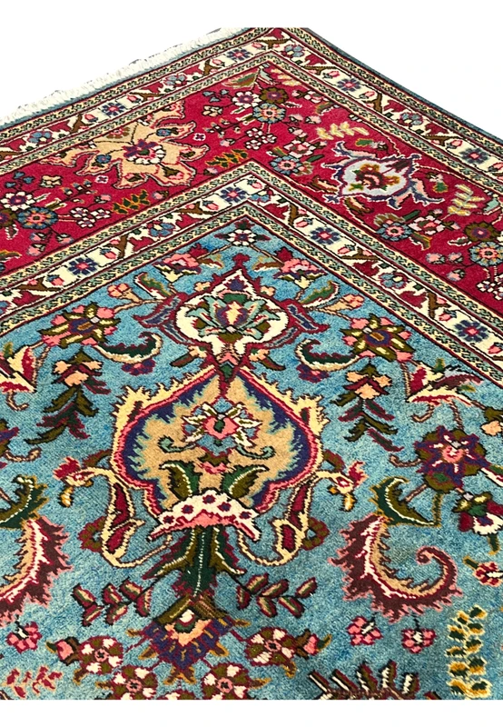 Upper edge of 10x13 Persian Tabriz rug, crimson border meeting sky blue field with vase motif