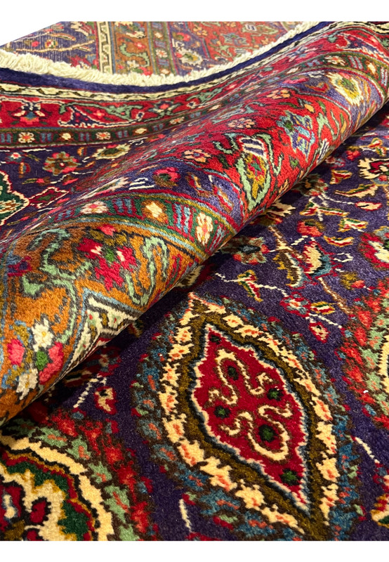 Rolled view of Persian Tabriz rug showing flexible hand-knotted wool pile and saturated jewel tone palette
