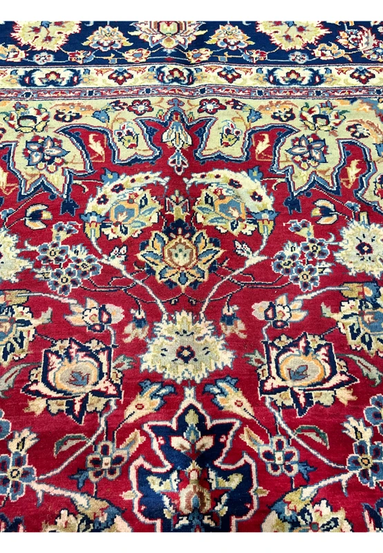 Upper field detail of Persian Isfahan rug showing top of medallion and ivory corner cartouche meeting deep red ground